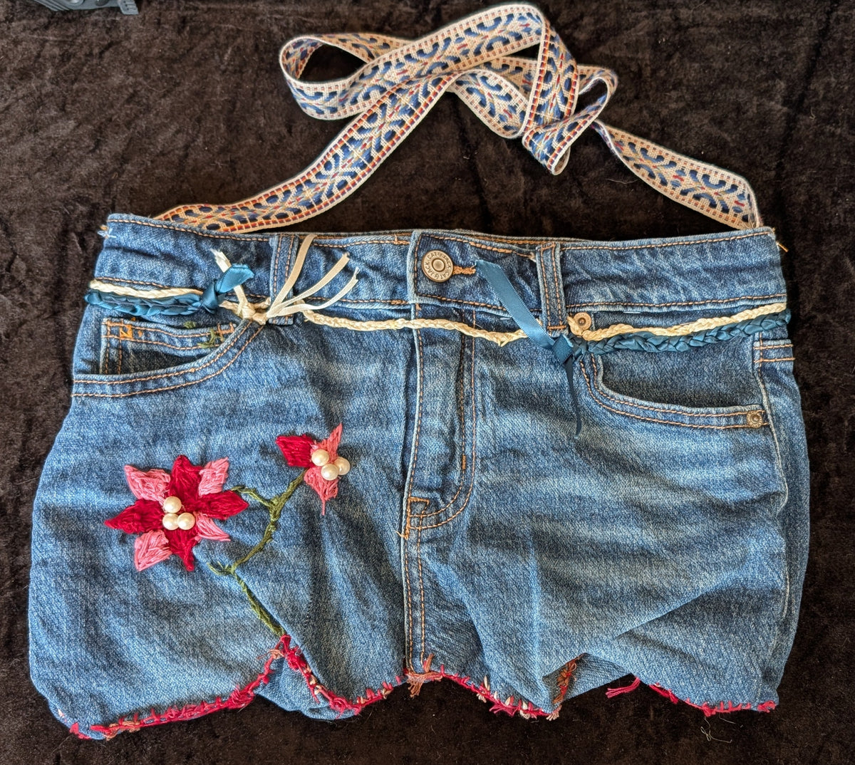 A pair of blue denim shorts crafted into hand sewn red and white floral embroidery with pink trim